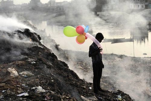 Một cậu bé đứng bên con sông ở thủ đô của Bangladesh. Xung quanh cậu khói mù mịt bốc lên từ những đống rác bị đốt cháy (Ảnh: SAI)