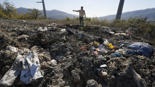Một người dân trong làng cạnh đống rác và đất đá (Ảnh: AP)