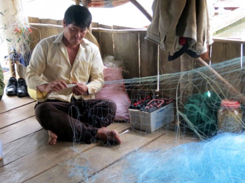 Anh Nguyễn Văn Diên, 48 tuổi ở ngay đầu làng chài trên lòng hồ thủy điện Đồng Nai 3 vá lưới để kịp chuyến bắt cá khi màn đêm buông xuống (Ảnh: Nhân Dân)