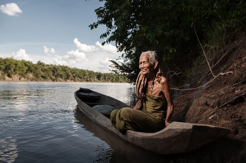 Một bà lão tại làng Kbal Romeas đang ngồi trên một chiếc ghe gỗ vốn rất phổ biến trên sông Srekok. Hầu hết dân làng đã rời đi, những chiếc ghe này hiếm khi còn được dùng để đánh bắt cá, thay vào đó, chúng được dùng để những người già bám vào tắm sông. (Ảnh: Giorgio Taraschi/Al Jazeera)